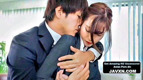 Japanese man in suit passionately hugs and kisses brunette woman's neck in office blouse