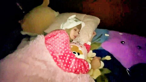 Cute petite girl sleeping in pink polka-dot cat pajamas with plush toys