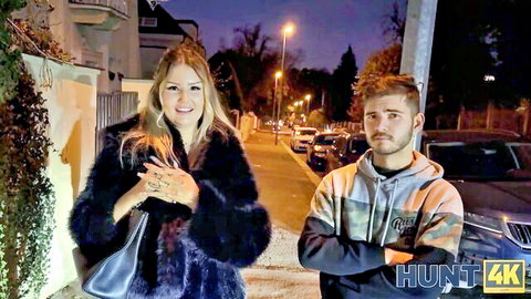 Smiling blonde in sexy fur coat stands with boyfriend on night street
