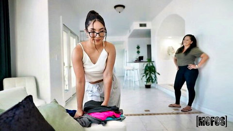 Petite brunette in glasses bends over white tank top showing cleavage and small ass in sweatpants grabbing clothes with friend watching