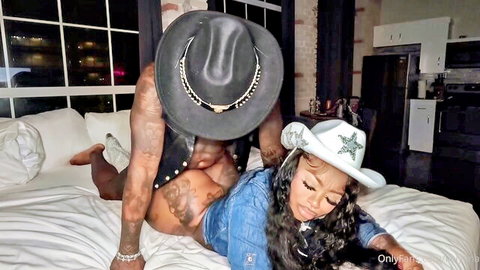 Keiyana in white cowboy hat with tattooed black partner in black hat on bed
