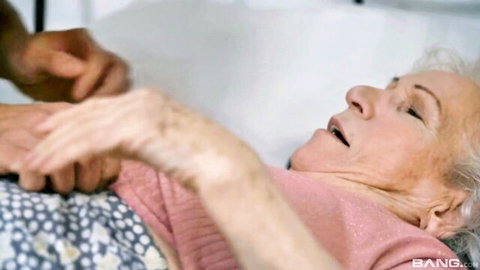 Granny moaning with open mouth as black hand gropes her arm and body through pink nightgown on bed