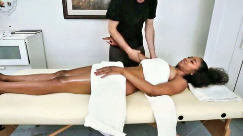 Ebony babe lies nude on massage table as white masseur rubs her bare back and side tits