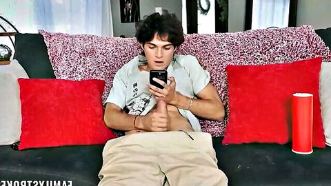 Young guy strokes his hard cock while watching phone on colorful couch