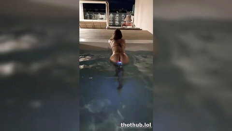 Curvy brunette bends over in outdoor rooftop pool showing juicy ass in tiny white thong bikini
