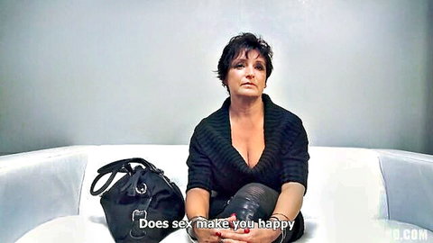 Mature brunette MILF teases with deep cleavage tits in low-cut sweater on couch POV