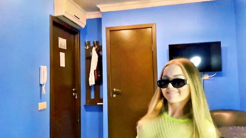 Smiling blonde teen in sheer green top and sunglasses teasing in bedroom