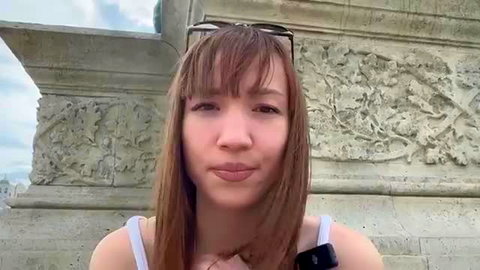 Sexy French brunette with bangs smiling at Arc de Triomphe in tank top