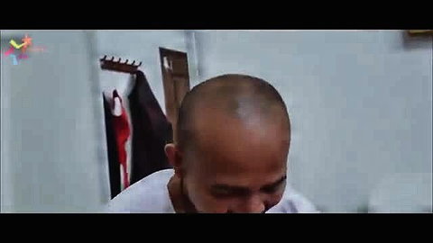 Bald Asian man in white shirt gazes down in intimate bedroom scene