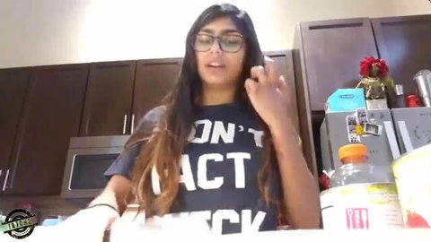 Mia Khalifa in kitchen wearing Don't Act Thick t-shirt, smiling at camera