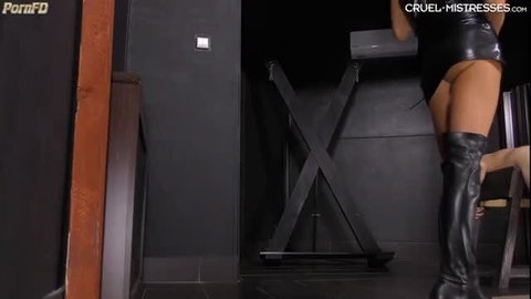 Mistress Ariel in latex dress and thigh boots dominates sub in BDSM studio