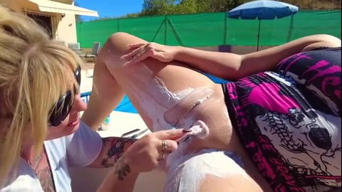 Blonde woman shaving another woman's pussy by the pool