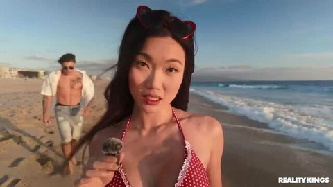 Lucy Mochi in red polka dot bikini walking on sunny beach