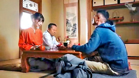 Japanese woman in orange top sits with two men around low wooden table in tatami room