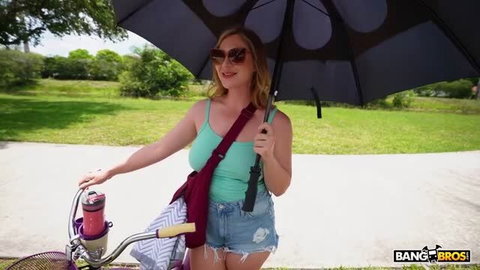 Voluptuous blonde in denim shorts holding umbrella by bike