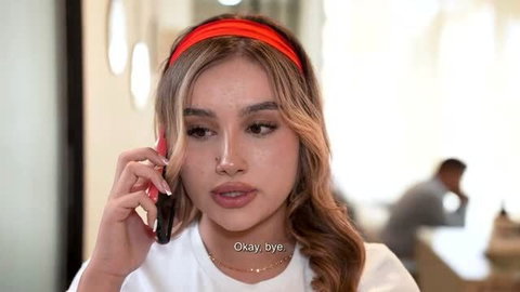 Kate Rous on phone wearing orange headband, white top