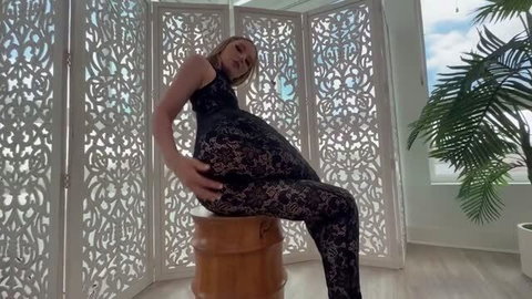 Abbie Sykes pregnant in black lace dress, posing seductively on wooden stool