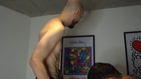 Bald muscular man standing shirtless in front of Keith Haring and Keith Haring art prints