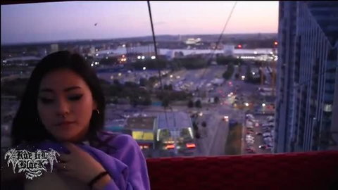 Rae Lil Black in purple top overlooking city at dusk