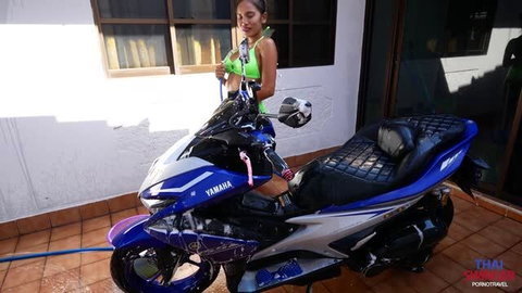 Asian woman in green bikini washing blue Yamaha motorbike