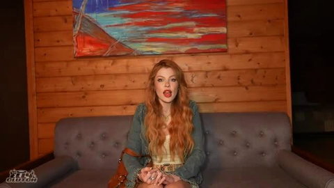 Elly Clutch redhead model sitting on couch with long wavy hair and green outfit