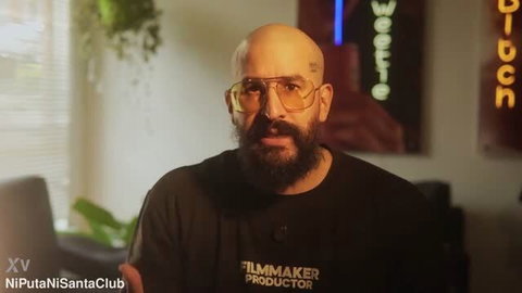 Bald bearded man with sunglasses and face tattoos in black FILMMAKER shirt
