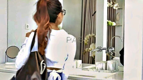 Rae Lil Black in white cropped top and glasses, ponytail tease in mirror