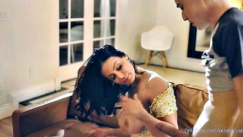 Kendra Lust in off-shoulder yellow dress, teasing touch on couch