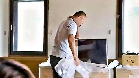 Housewife watches man in white shirt unpack large TV screen from bubble wrap in home
