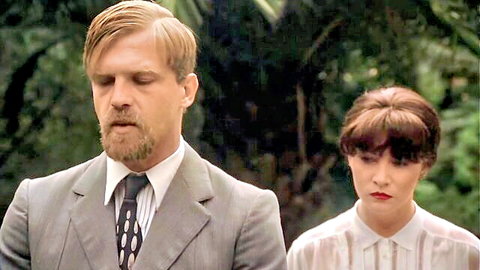 Blonde bearded man in suit with brunette woman in white blouse in jungle setting