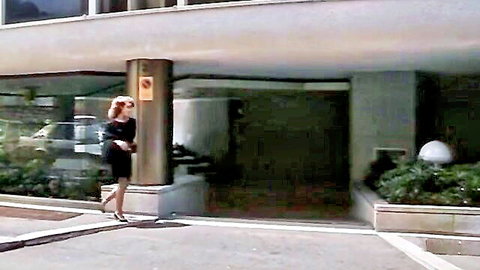 Blonde woman in short black dress and heels entering building at night
